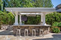 035 - 19 Warwick Court - Outdoor kitchen with a stone bar, metal stools, and a covered grill area