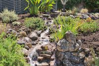 031 - 3165 Lucas Drive - Tiered rock water feature surrounded by lush landscaping and garden greenery.