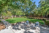 039 - 119 - 2116 Stewart Avenue - Backyard patio with two white chairs overlooking a large green lawn surrounded by trees and landscaping
