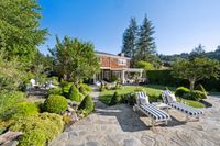 50 - 231 Sundown Terrace - landscaped backyard with stone pathways, manicured greenery, lounge chairs, and a patio dining area extending from a charming two-story home.