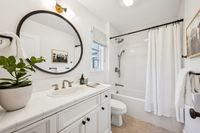 38 _ 910 Carl Road _ Bright bathroom with white vanity, round mirror, and a tub-shower combo with classic tile surround.